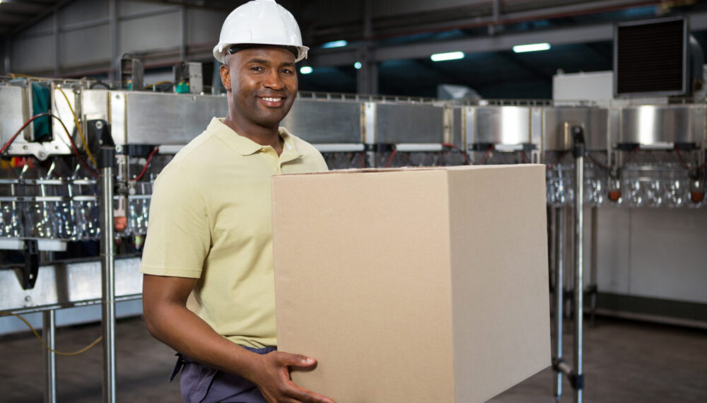 Portrait of smiling male employee carrying cardboard box in juice factory