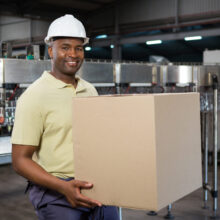 Portrait of smiling male employee carrying cardboard box in juice factory