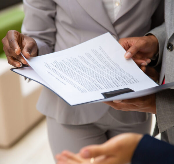 Diverse business partners reading contract together Diverse business partners reading contract together. Business man and woman wearing formal suits, standing and holding open folder with document. Agreement concept