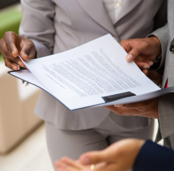 Diverse business partners reading contract together Diverse business partners reading contract together. Business man and woman wearing formal suits, standing and holding open folder with document. Agreement concept